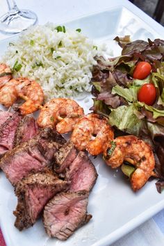 a white plate topped with meat and veggies next to rice on a table