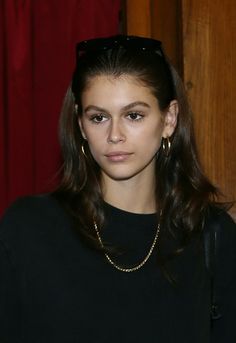 a woman with long hair wearing sunglasses and a black shirt is standing in front of a red curtain