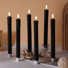 five black candles are lined up on a table next to a cup and saucer