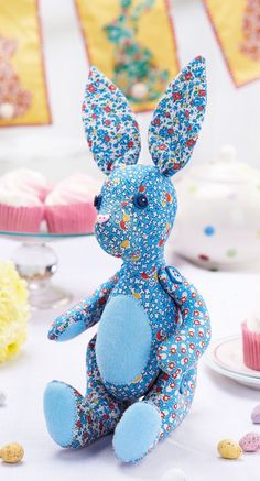 a blue stuffed animal sitting on top of a table next to cupcakes and cake