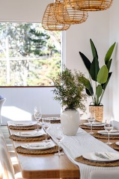 a dining room table set with place settings and place settings for the dinner table, next to a potted plant