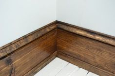 the corner of a room with wood flooring and white painted walls, along with wooden planks