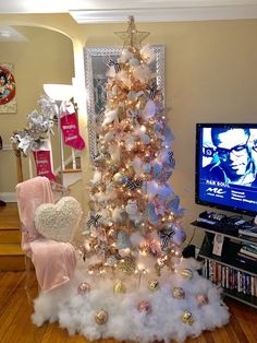 a white christmas tree with pink and gold ornaments in front of a flat screen tv