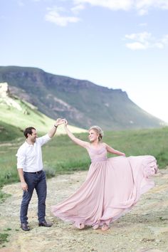 a man and woman holding hands while standing on a dirt road