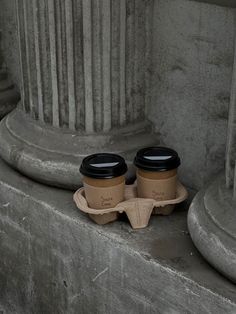 two cups of coffee sitting on top of each other next to some concrete pillars and columns