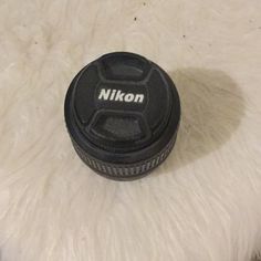 a nikon lens cap sitting on top of a white fur covered floor next to a black camera