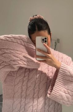 a woman taking a selfie with her cell phone while wearing a pink cable knit sweater