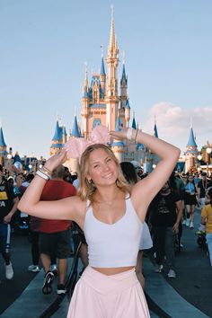 a woman standing in front of a castle with her hands on her head and arms behind her head