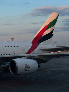 a large jetliner sitting on top of an airport tarmac at sunset with clouds in the background