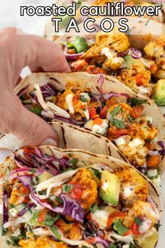 two tacos filled with chicken and vegetables on top of a white plate next to a hand holding a tortilla