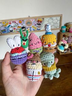 small crocheted toys are being held up in front of a wall with pictures on it