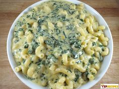 a white bowl filled with macaroni and cheese covered in spinach on top of a wooden table