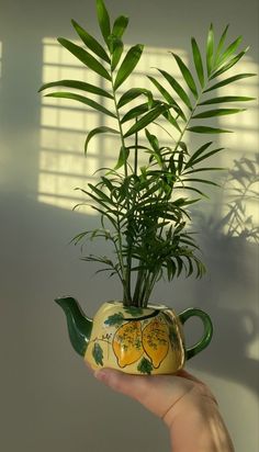 a hand holding a potted plant in the shape of a teapot with lemons painted on it