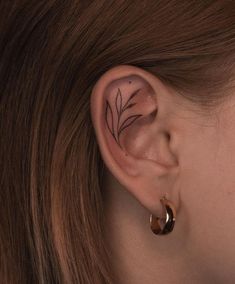 a woman's ear with a small leaf tattoo on the left side of her ear