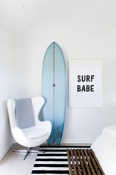 a bedroom with a surfboard on the wall next to a white chair and bed