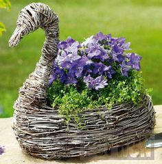 a bird made out of twigs with purple flowers in the front and green grass behind it