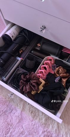 an open drawer with clothes, hairdryers and other items in it on a pink rug