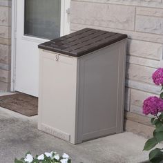 a trash can sitting on the side of a building next to some flowers and bushes