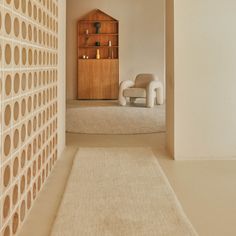 an empty room with a white rug on the floor and a book shelf in the corner