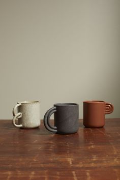 three different colored mugs sitting on top of a wooden table next to each other