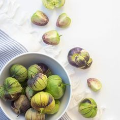 a bowl filled with green and purple fruit on top of a white table cloth next to other fruits