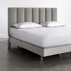 a bed with white sheets and pillows on top of it in a gray floored room