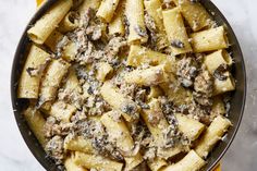 a skillet filled with pasta and mushrooms on top of a marble countertop next to a yellow towel