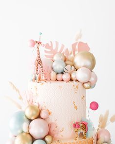 a pink and gold cake with giraffes, balloons, and other decorations