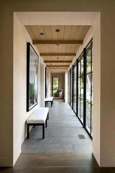 a long hallway with benches and windows on both sides, leading to an outside sitting area