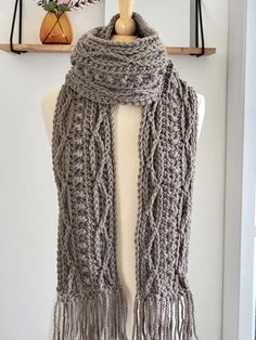 a gray knitted scarf hanging on a wooden shelf next to a vase with flowers