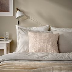 a bed with white sheets and pillows on top of it next to a night stand