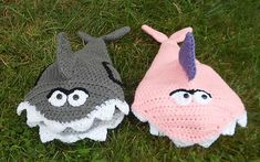 two crocheted hats sitting on top of green grass next to each other with eyes