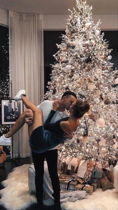 a man and woman kissing in front of a christmas tree