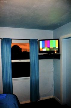 a tv sitting on top of a window sill next to a blue bed in a room