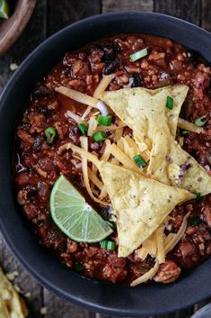 a bowl filled with chili and tortilla chips on top of a wooden table