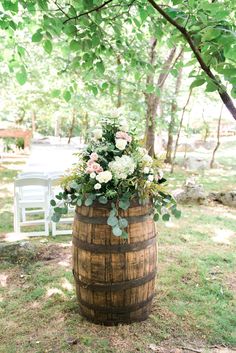 a wooden barrel with flowers and greenery on the ground in front of a white chair