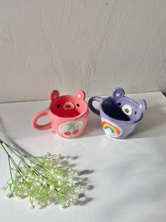 two ceramic cups sitting next to each other on a white surface with flowers in the foreground