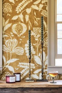 two candles are sitting on a table next to a wall with a flower pattern and some other items