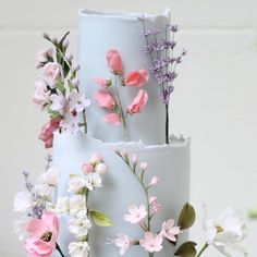 a three tiered white cake with pink and purple flowers on it's side