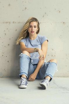 a young woman sitting on the ground with her legs crossed and looking at the camera