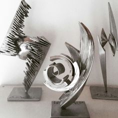 three metal sculptures sitting on top of each other in front of a white wall and floor