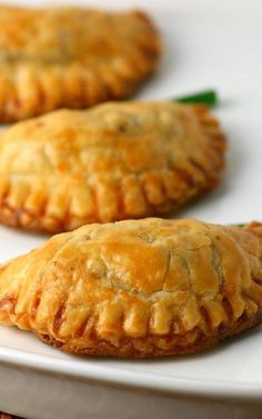 three small pastries on a white plate with green garnishes next to them