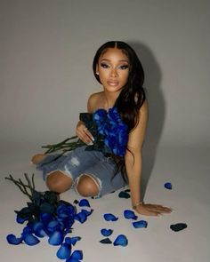 a barbie doll sitting on the ground with blue flowers in front of her and petals all around her