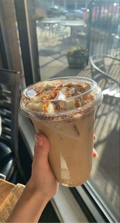 a person holding up a drink in front of a window