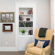 a living room with a chair, bookshelf and pictures hanging on the wall