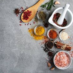 spices and seasonings are arranged in bowls on a gray surface with wooden spoons