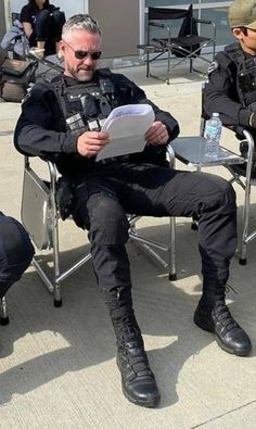 two police officers are sitting in chairs and one is reading a paper while the other sits down