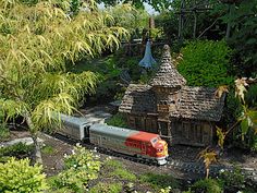 a toy train is coming down the tracks in front of a small house and trees