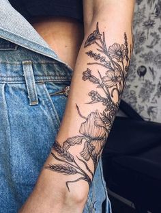 a woman's arm with flowers on it and a blue jean jacket in the background