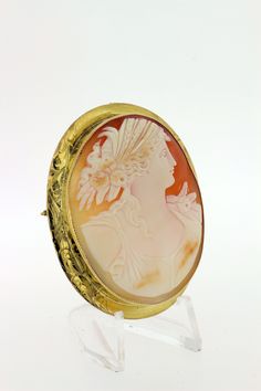 This delightful cameo brooch is made in 14K yellow gold and oval cut cut piece with a Greek motif with a female figure. She's detailed with braided hair, feathers, and roses. The brooch is accented with an engraved bezel and migraine edge. It can also be worn as a necklace too--has a toggle that can flip up or down. The entire piece measures 57mm long, 46.31mm wide, 11.33mm tall, and weighs 10.7DWT. B55KIPPN --Please reference our policy for more details before purchase-- For International order Luxury Oval Cameo Brooch, Gold Oval Carved Brooches, Oval Carved Gold Brooches, Luxury Oval Intaglio Brooches, Heirloom Oval Brooches With Intaglio, Luxury Oval Engraved Brooches, Yellow Gold Oval Cameo Brooch, Hair Feathers, Convertible Necklace